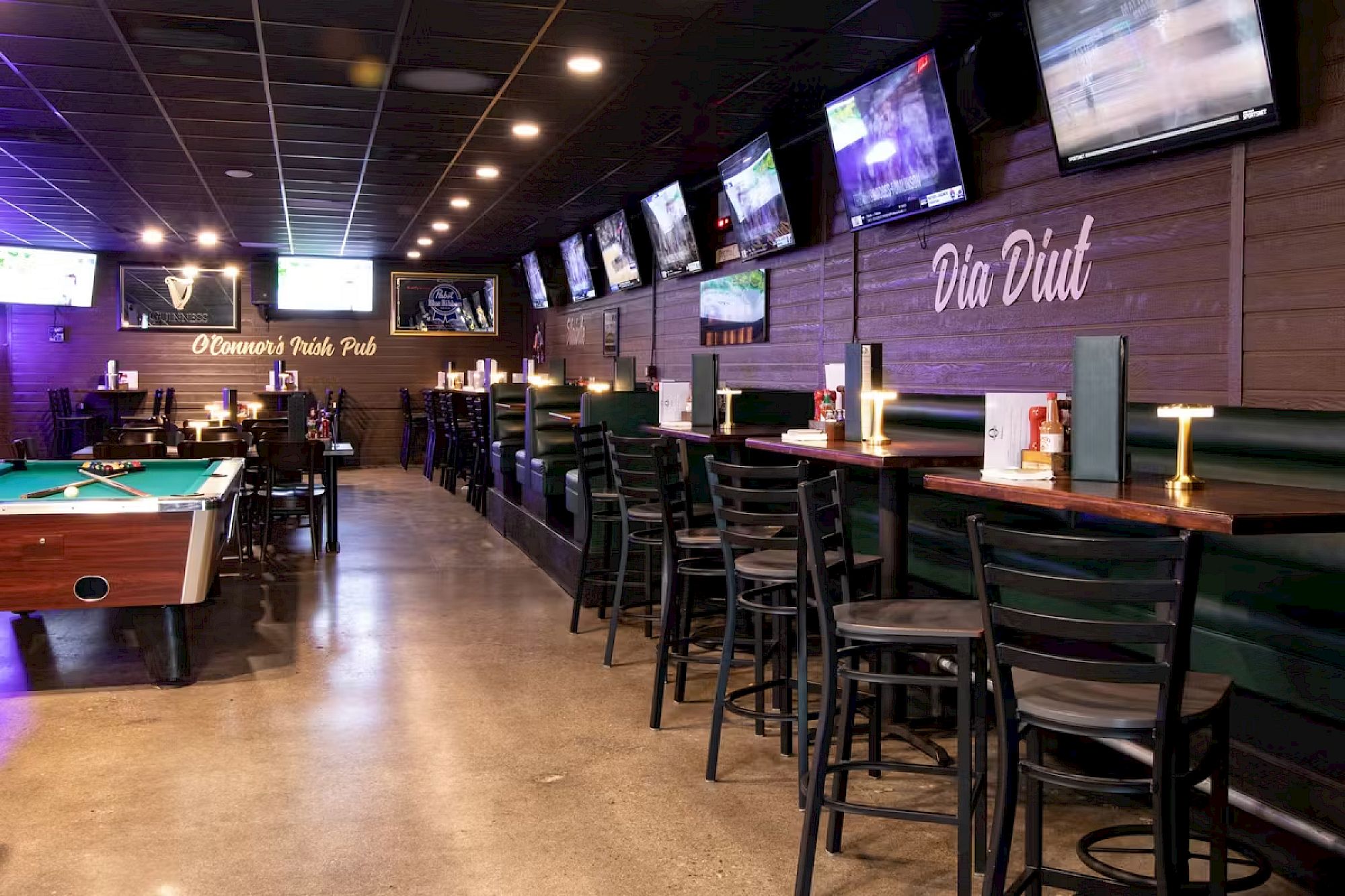 The image shows the interior of an Irish pub with bar stools, tables, a pool table, and multiple TVs mounted on the wall displaying sports channels.