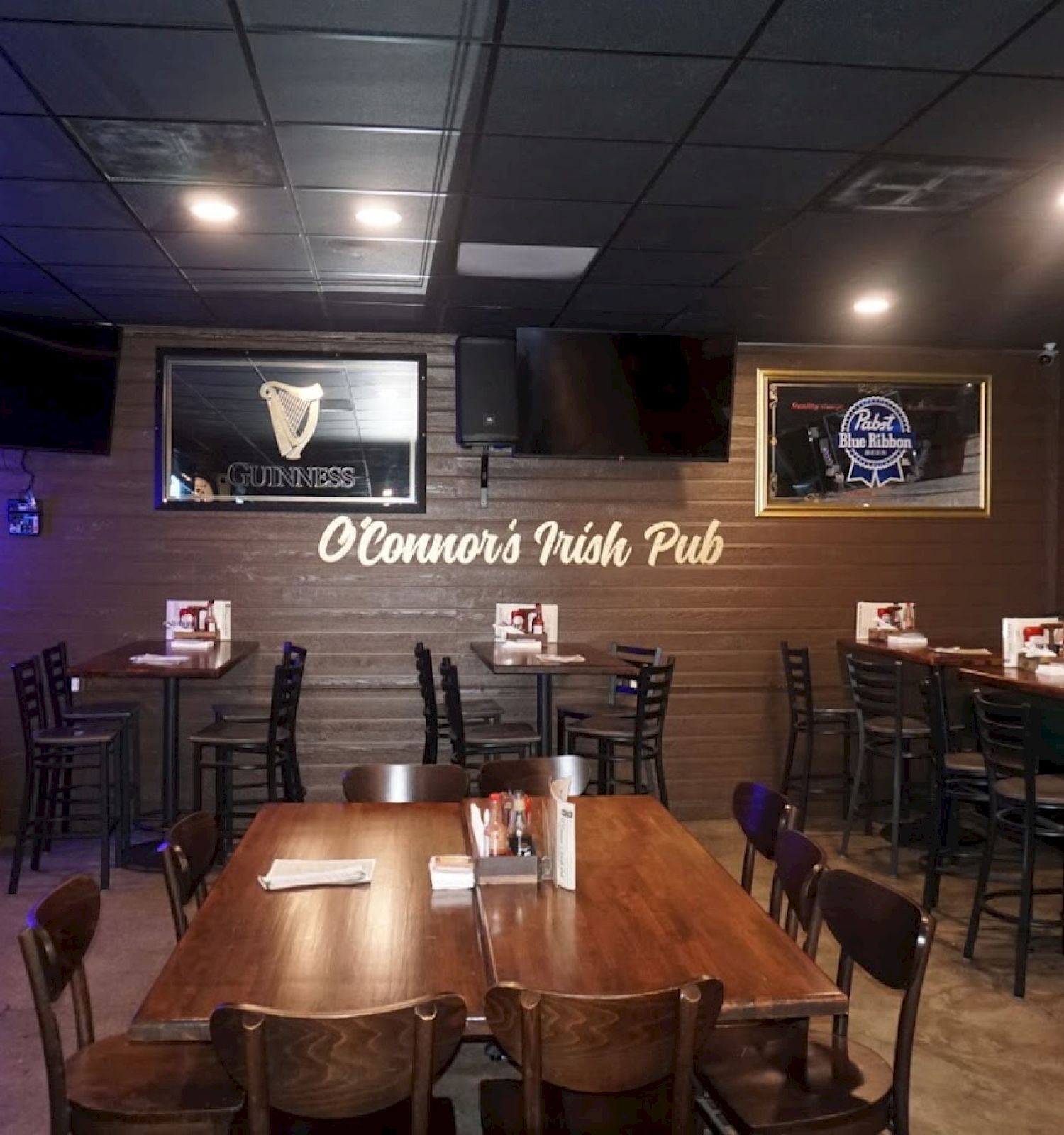 A cozy Irish pub with tables, chairs, and wall decorations, including TV screens. The sign reads 