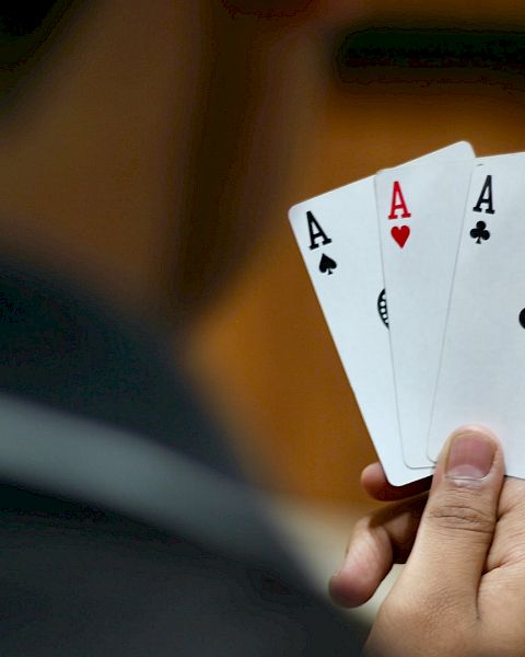 A person is holding three playing cards: Ace of Spades, Ace of Hearts, and Ace of Clubs. Their hand is positioned so the cards are clearly visible.