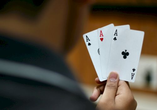 A person is holding three playing cards: Ace of Spades, Ace of Hearts, and Ace of Clubs. Their hand is positioned so the cards are clearly visible.