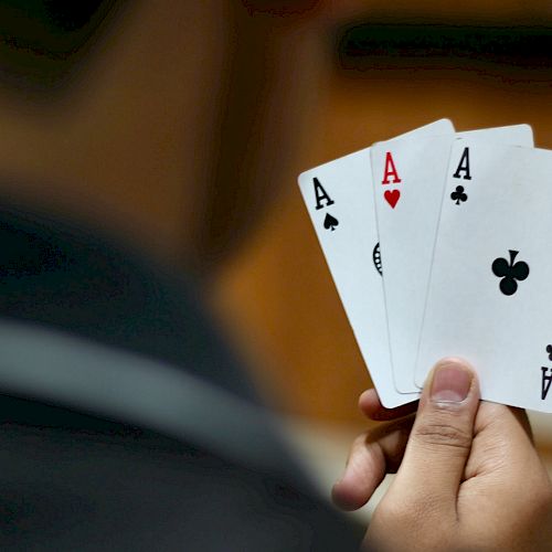 A person is holding three playing cards: Ace of Spades, Ace of Hearts, and Ace of Clubs. Their hand is positioned so the cards are clearly visible.