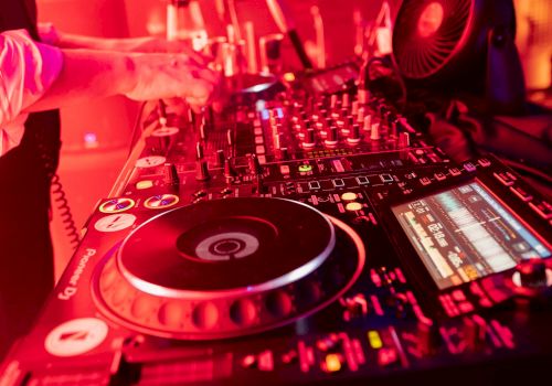 The image shows a DJ setup with turntables, a mixer, and a laptop, all illuminated by red lighting, featuring equipment branded 